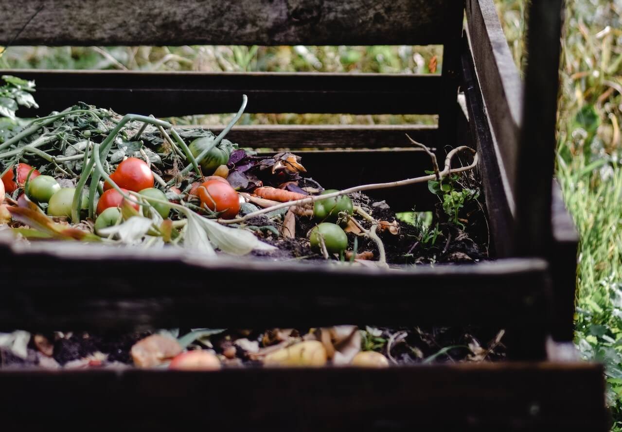 Ein hölzerner Kompostbehälter, der mit sich zersetzenden Pflanzen und Lebensmittelabfällen gefüllt ist und das natürliche Recycling fördert.